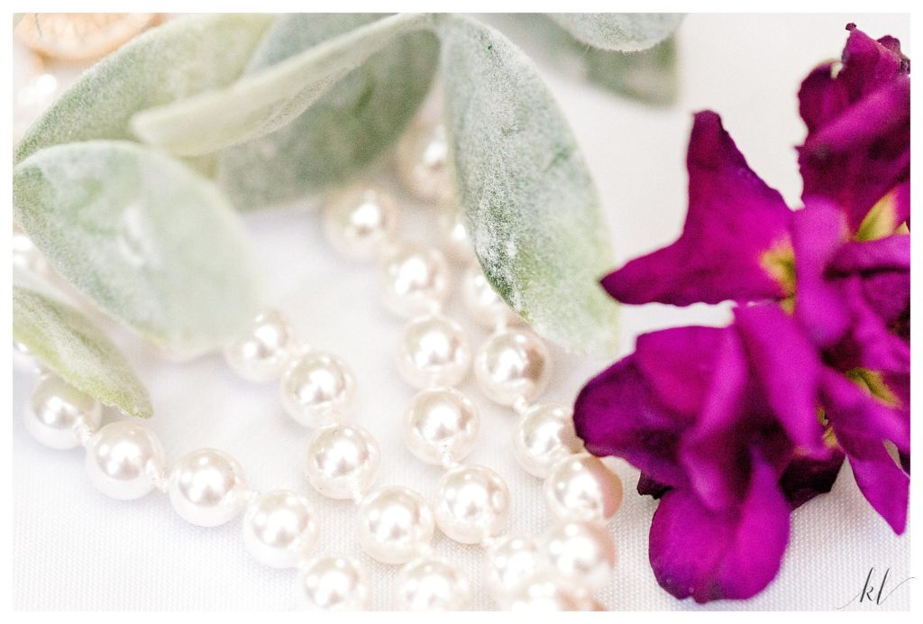 White pearls with a purple flower and greenery. 