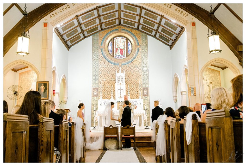 Bride and groom stand near the alter of a Dark Catholic church during their wedding ceremony.