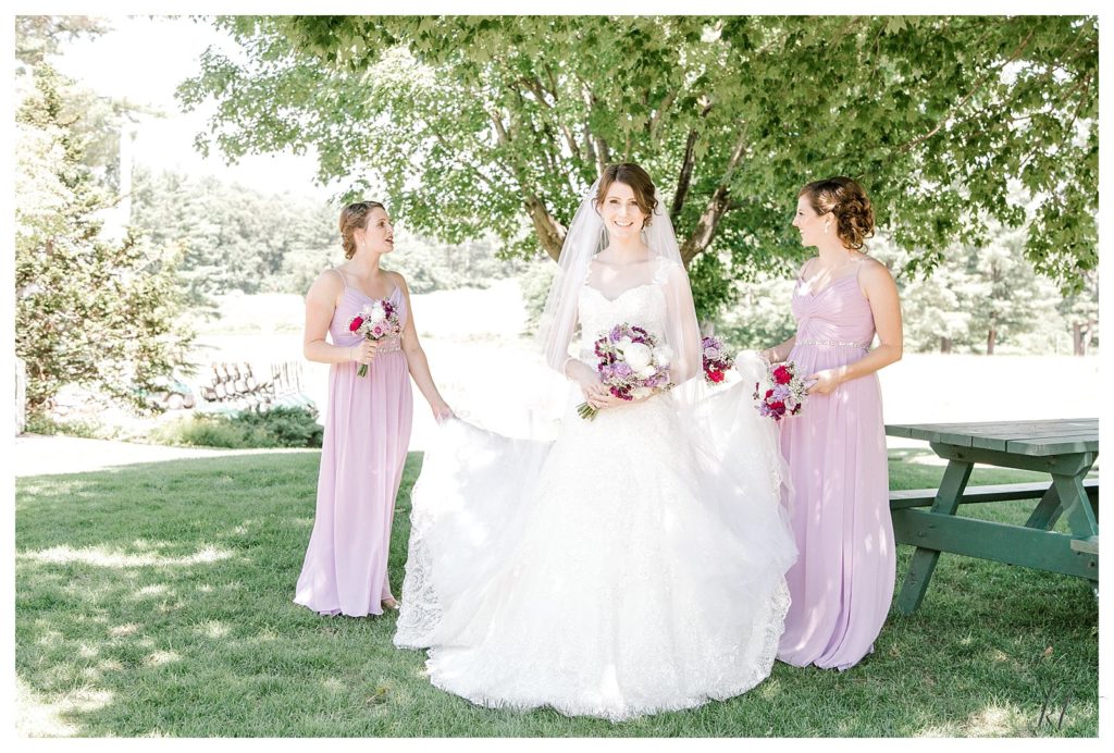 Two Bridesmaids wearing purple dresses hold Bride's dress at a Summer Wedding at the Keene Country Club. 