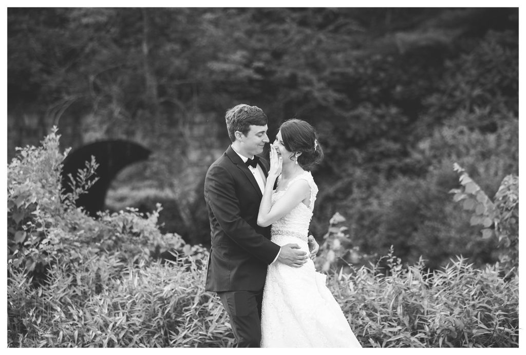 Black and White Candid photo of a bride and groom laughing together in front of the stone arch at the Keene Country Club. 