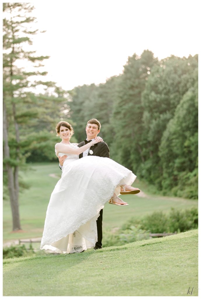 Groom scoops up his wife on a hill at the Keene Country club during the golden hour on their wedding day. 