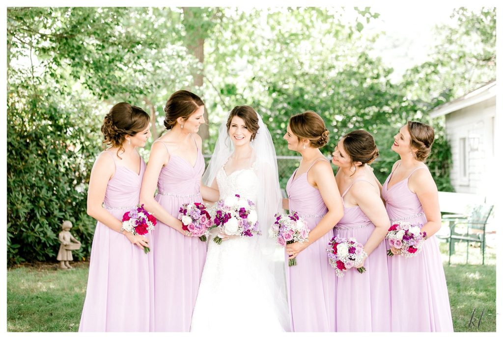 Formal portrait of a bride and her bridesmaids holding purple and white floral bouquets for her summer wedding at the Keene country club. 