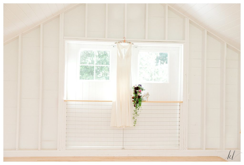 Simple white wedding dress hanging in a window at the new Event Barn at Mayfair Farm in Harrisville NH