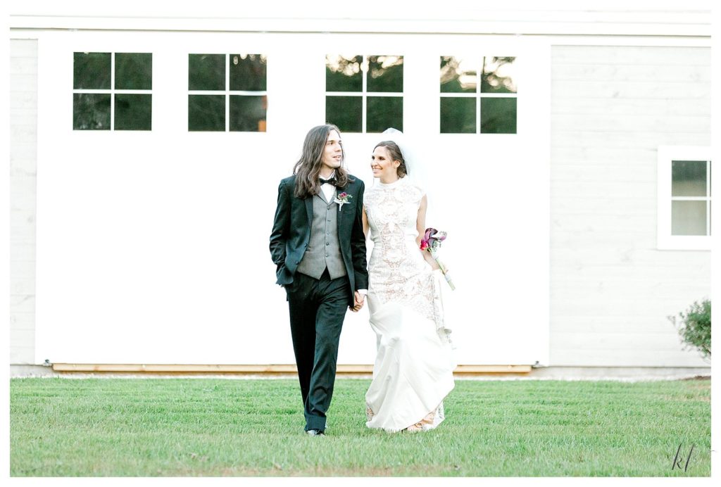 Candid photo of a bride and groom walking holding hands at their Wedding at Mayfair farm. 
