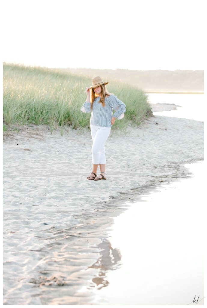 High School Senior photos taken on Drakes Island- on the shore.   Girl wearing white capris and a straw hat. 