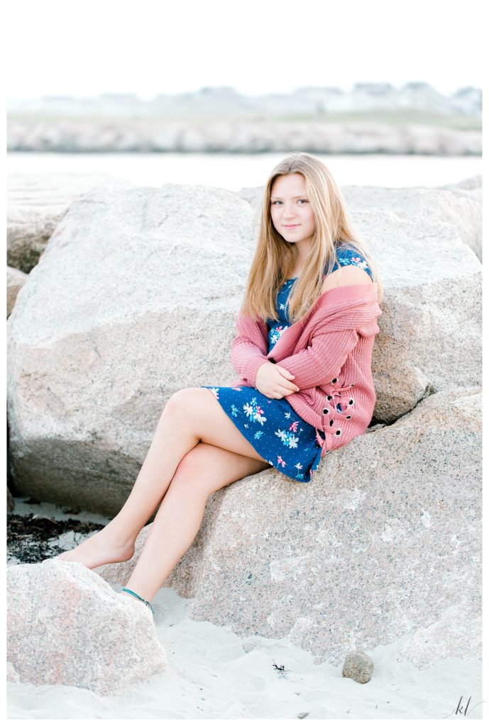 Drakes Island senior portrait of a girl wearing a pink sweater sitting on the rocks. 