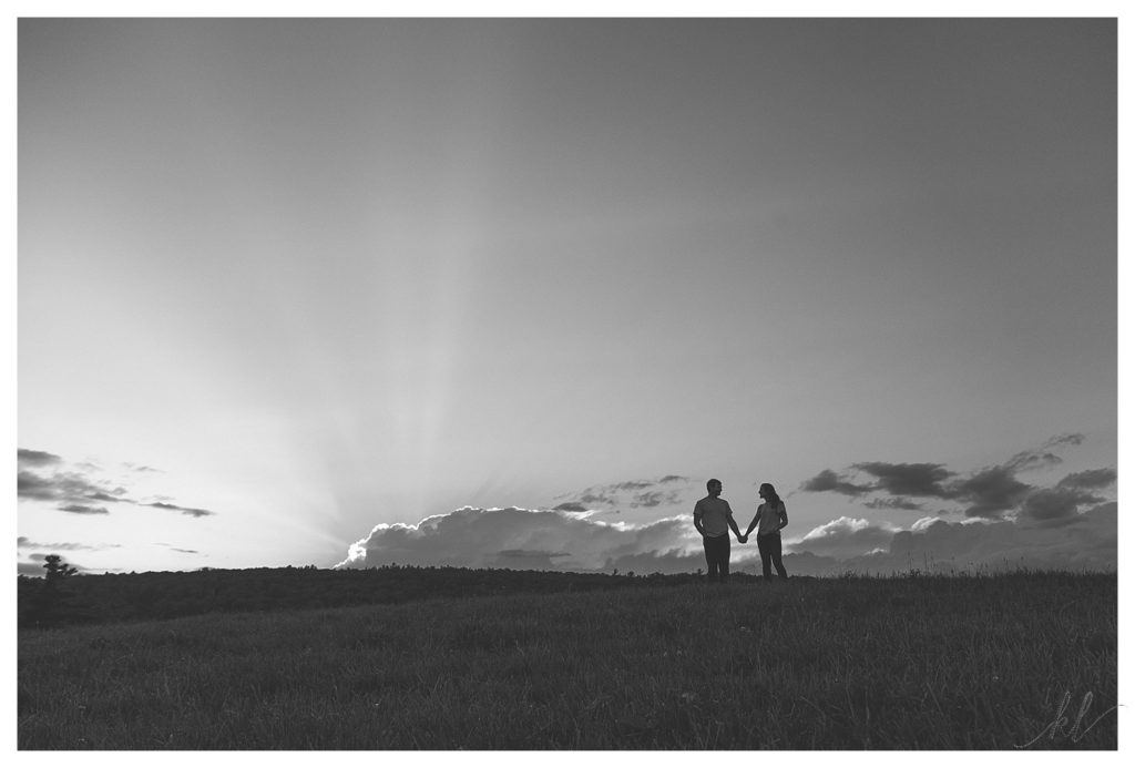 Black and white silhouette photo showing a man and woman holding hands in a field. 