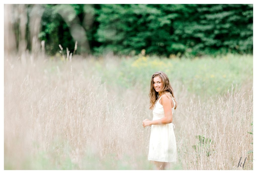 Light and Airy Senior Photo of a girl in a field of wheat-like grass wearing a soft yellow dress. 