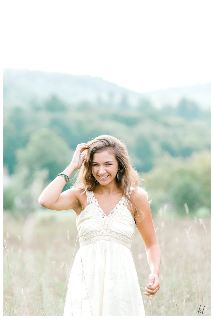 Light and Airy Senior Portrait of a girl wearing a pale yellow dress fixing her hair. 