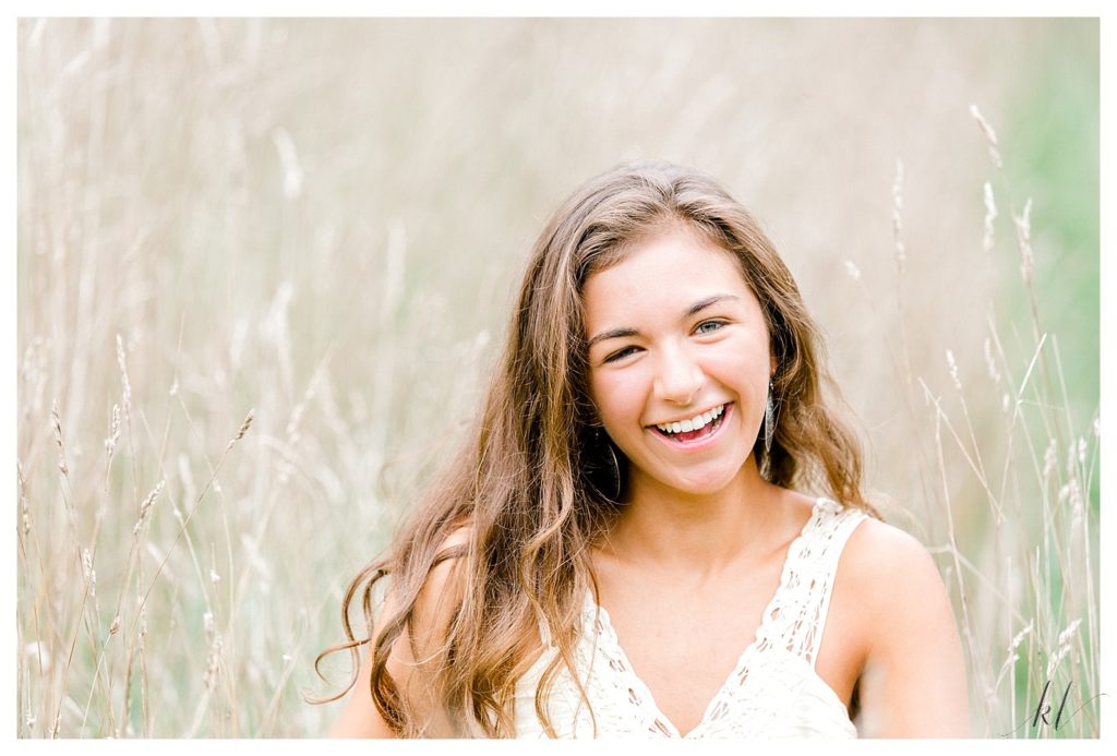 Senior photo of a girl smiling in a field of soft wheat grass. 