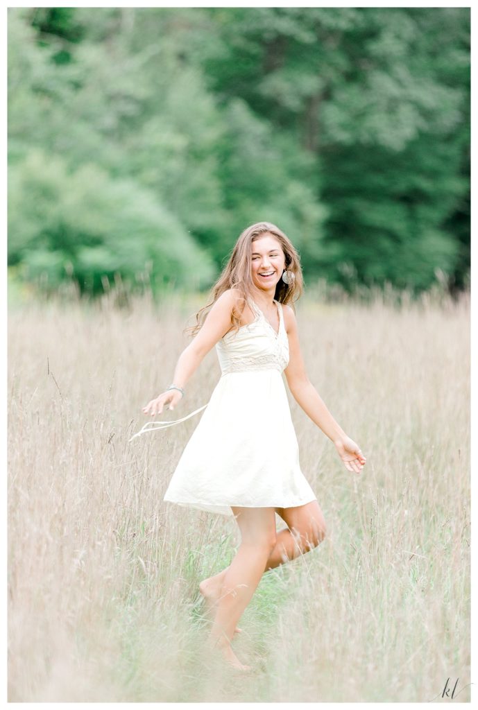 Fun and Candid light and Airy photo of a senior girl dancing in a field of wheat grass. 