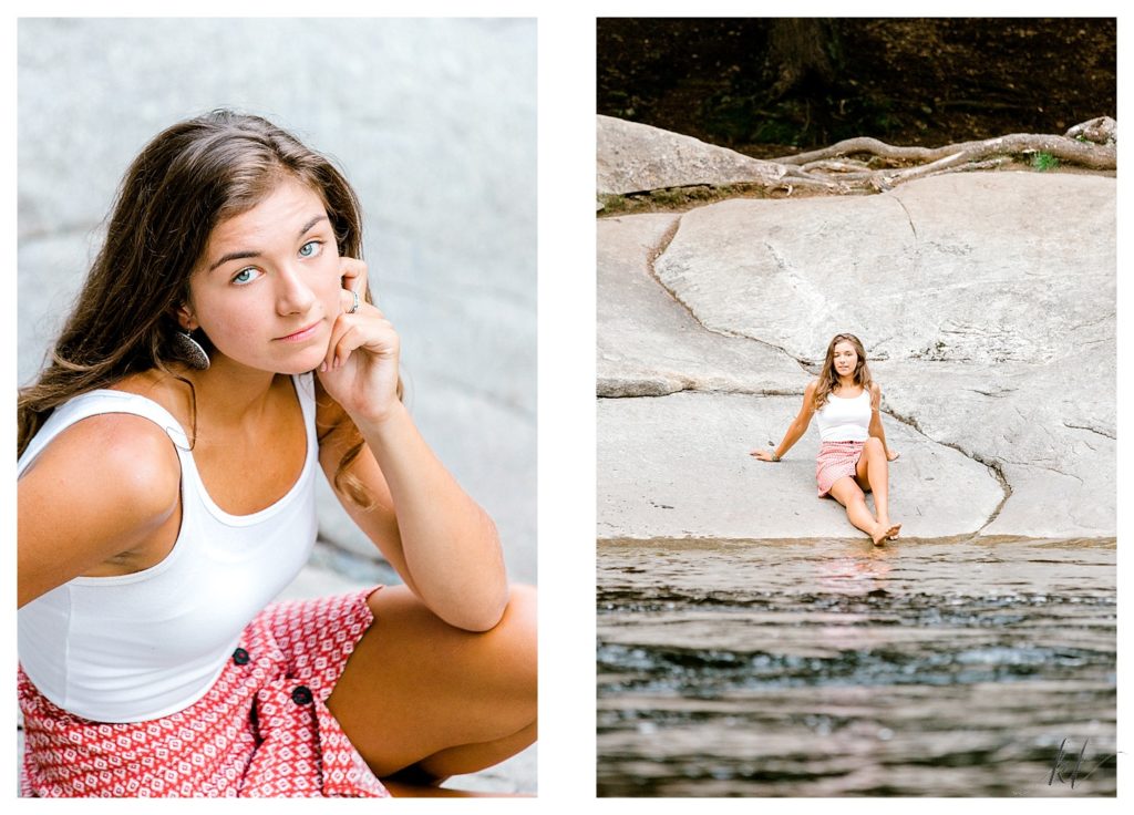 Senior Photos near a river. Girl in white tank-top and red patterned skirt sits on a rock near a river. 