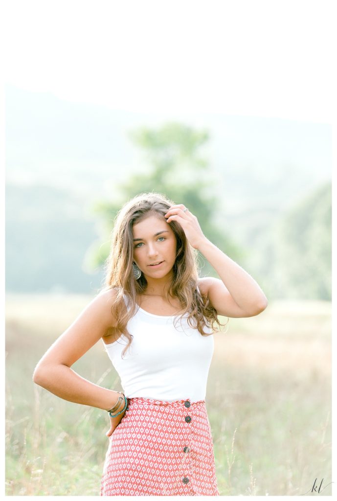 Girl poses for light and airy senior photos wearing a red and white patterned skirt with a white tank top