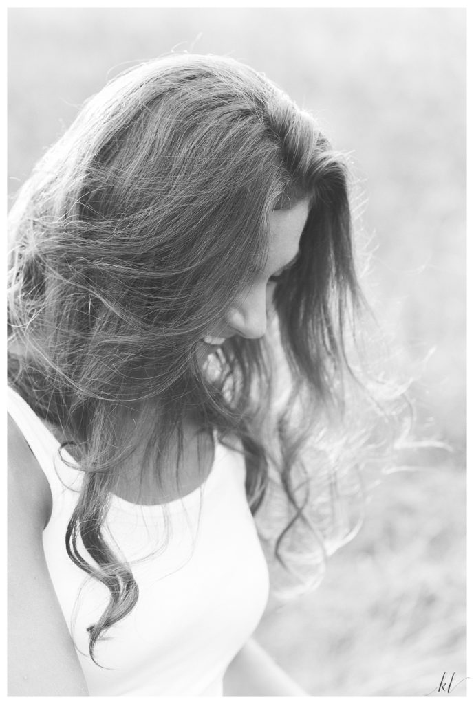 Candid black and white photo of a girl looking down and smiling, with her hair covering her face. 