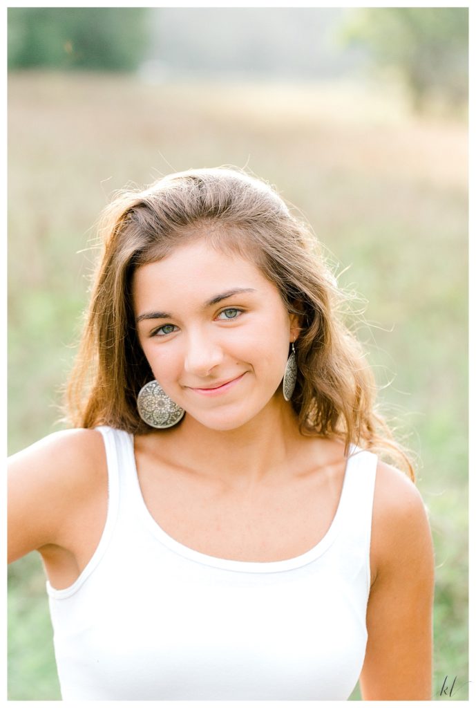 Head shot of a girl wearing a white tank top and silver, circular earrings. 