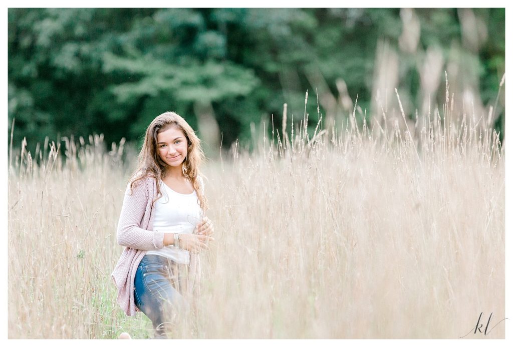 Light and Airy Senior Photos of a girl wearing jeans, white tank top and a pink sweater. 
