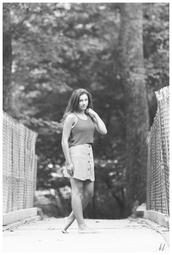 Black and White Looks like film photo of a senior girl standing on a wooden bridge. 