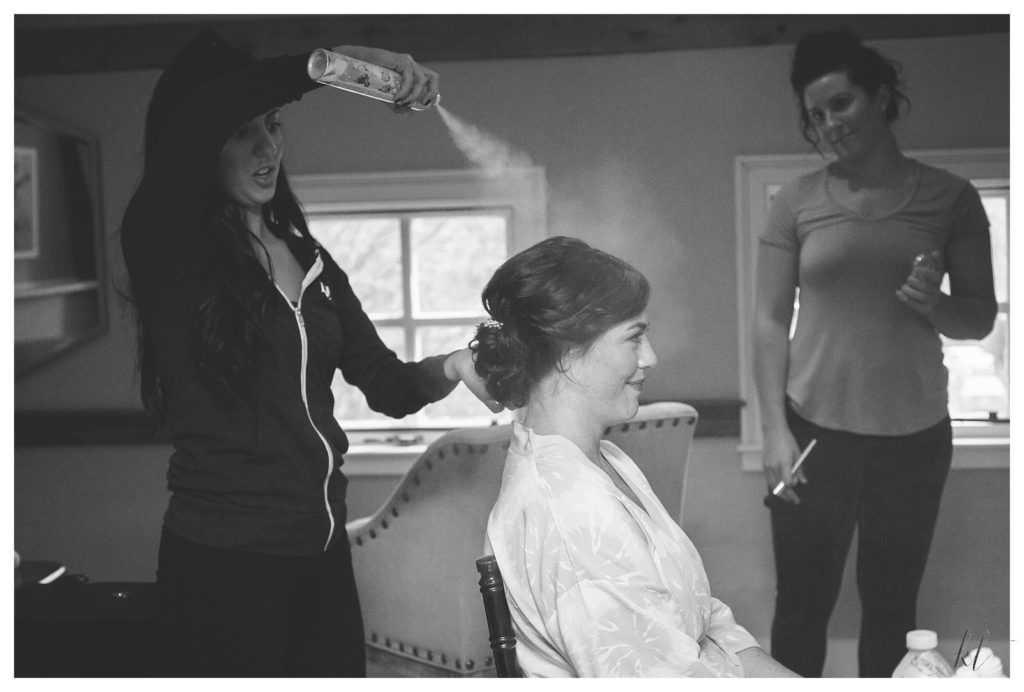 Black and white photo of a bride getting her hair sprayed by the stylist in the Wheeler Room at the Bedford village Inn. 