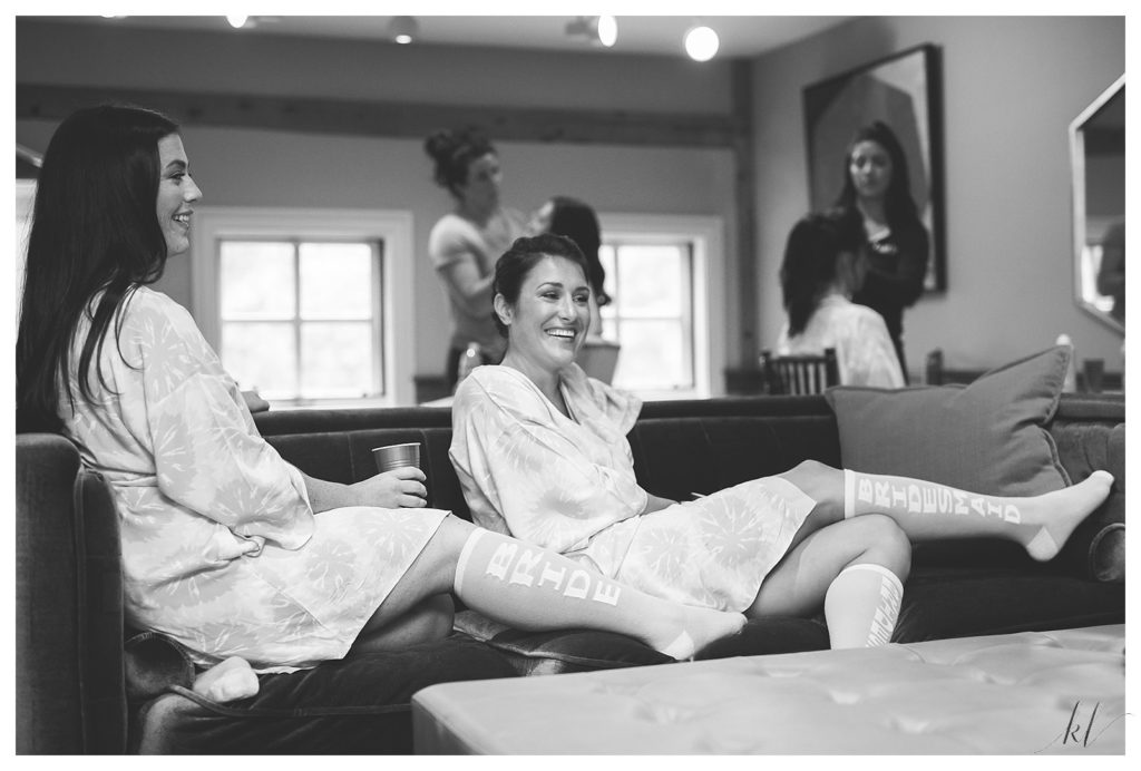 Black and white candid photo of a bride and bridesmaid wearing robes and custom knee high socks. 