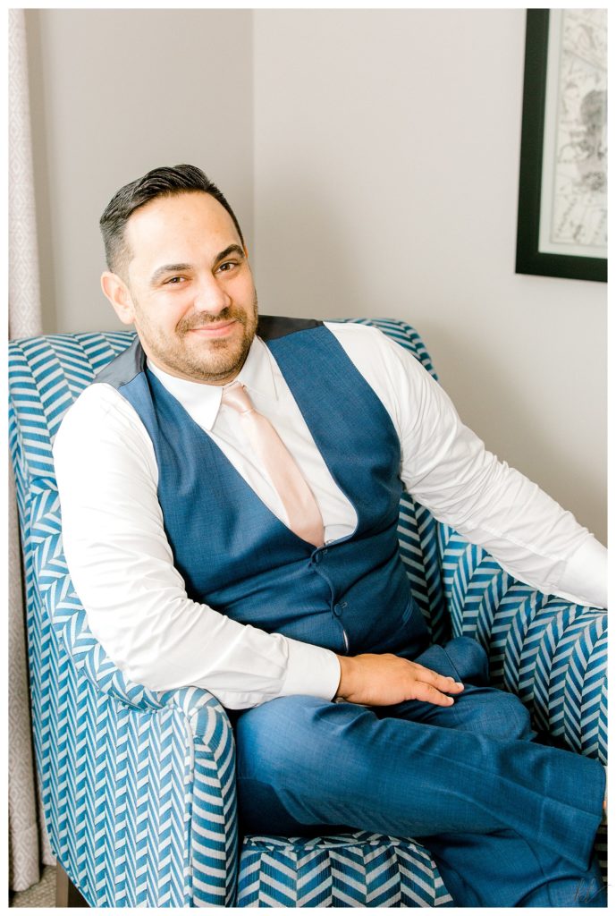 Groom sits in a chair on his wedding day. 