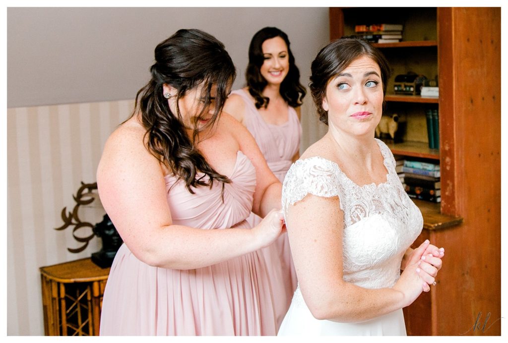 Maid of Honor wearing a pink dress- helps bride button her gown at the Bedford Village Inn. 