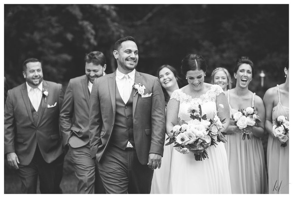 Black and White, Candid photo of bride and groom walking with their wedding party. 