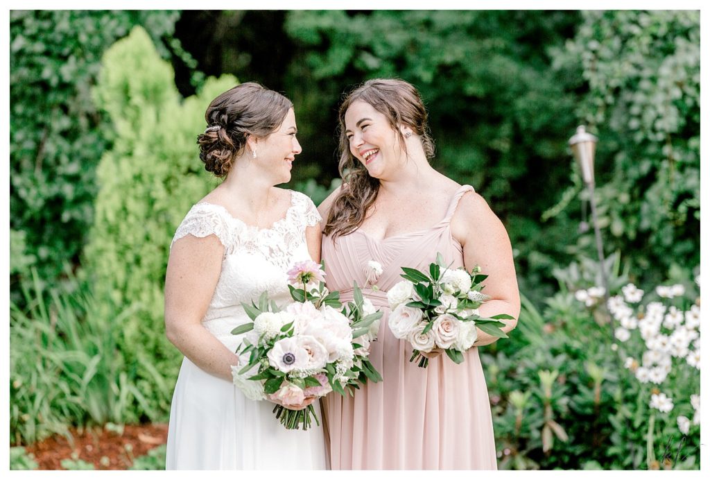 Bride wearing a lace topped Stella York Wedding gown is with her maid of honor in a dusty pink dress holding bouquets. 