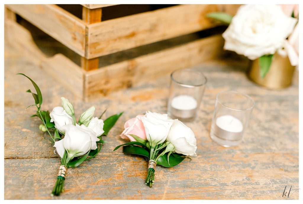 Boutonnieres with white flowers and gold metal tie on a rustic wood surface. 