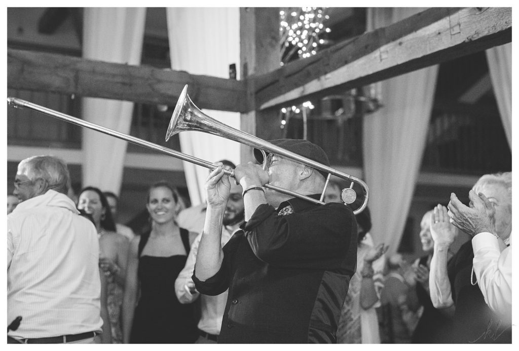 Black and White Photo of a "hot mess" band member playing the Trombone during a wedding reception. 