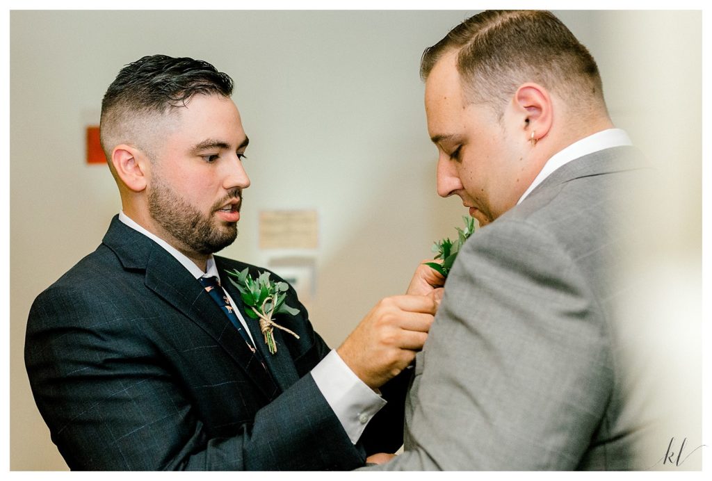 Groom helps pin boutonniere on his best man. 
