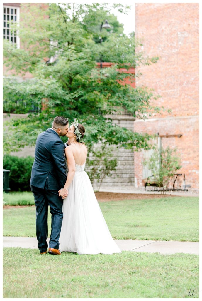 Bride and groom hold hands and kiss as they walk away from the photographer. Light and Airy photo by K. Lenox Photography