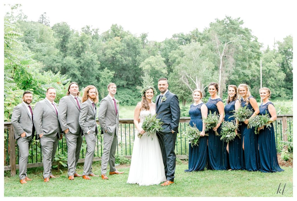 Wedding party posing for a portrait wearing grey suits, and blue dresses. 