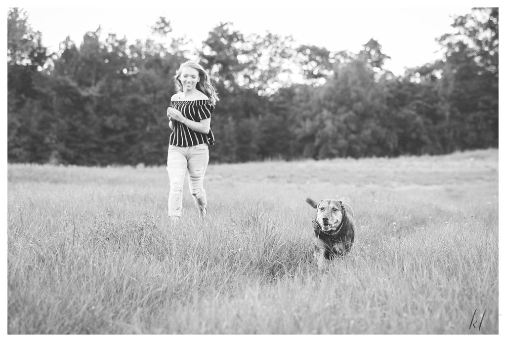 Black and White photo of a girl running and playing with her dog during her senior photos in West Chesterfield. 