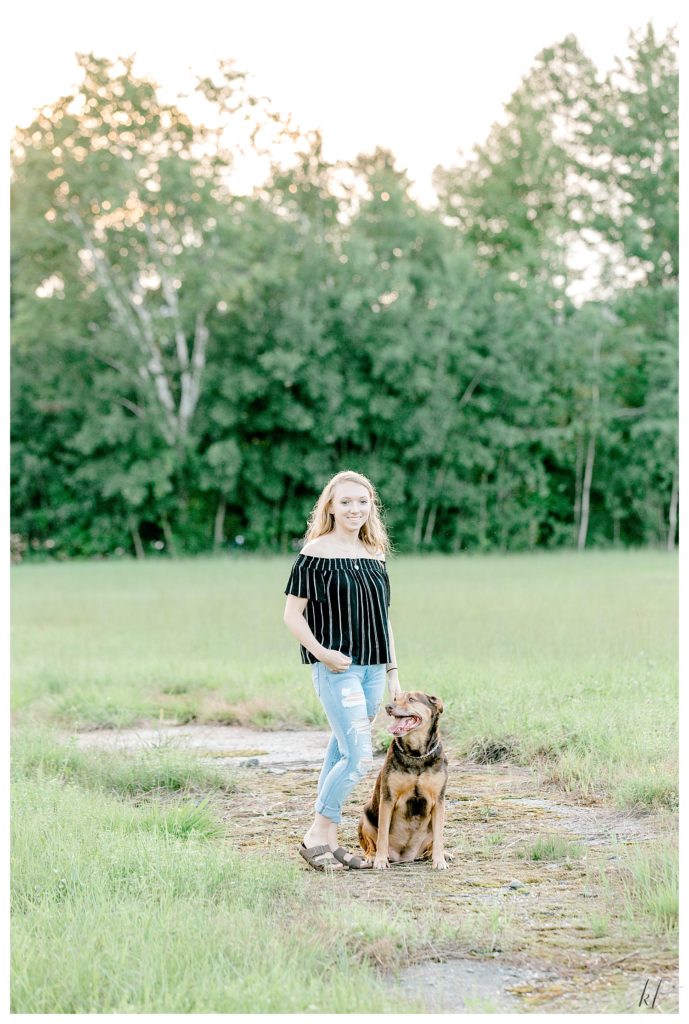 A girl wearing a striped black off the shoulder shirt- poses with her dog for senior portraits in West Chesterfield, NH.