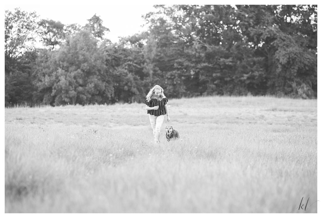 Black and White photo of a girl running in a field with her dog. 