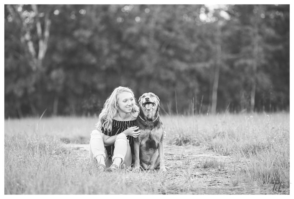 Black and white photo of a girl posing with her dog for her senior portraits in West Chesterfield. 
