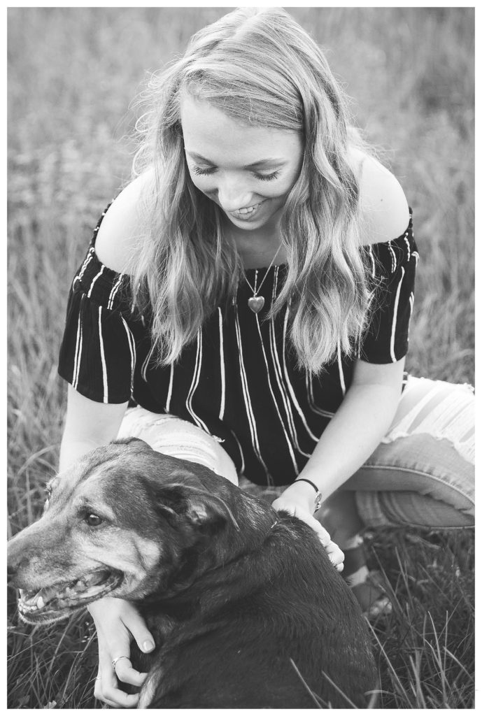 Black and White candid photo of a high school senior girl playing with her dog. 