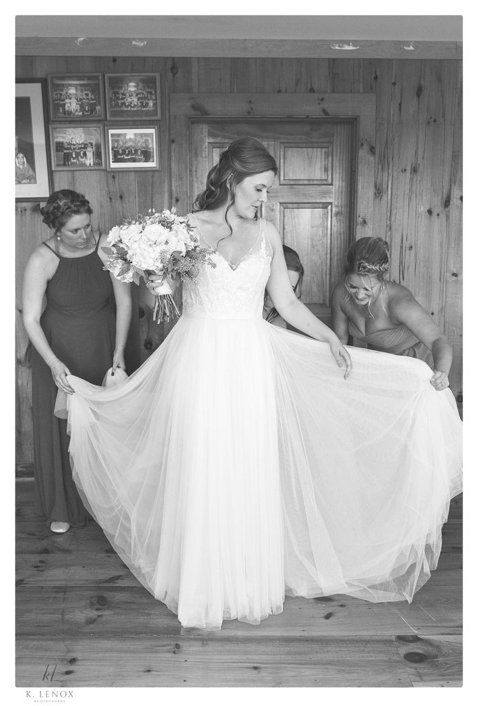 Black and white photo of a bride being helped into her dress by her bridesmaids. 