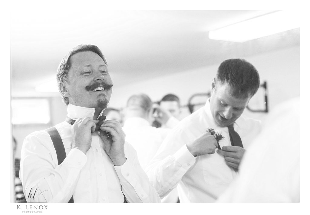 Black and white photo of a groom putting on his bowtie. 