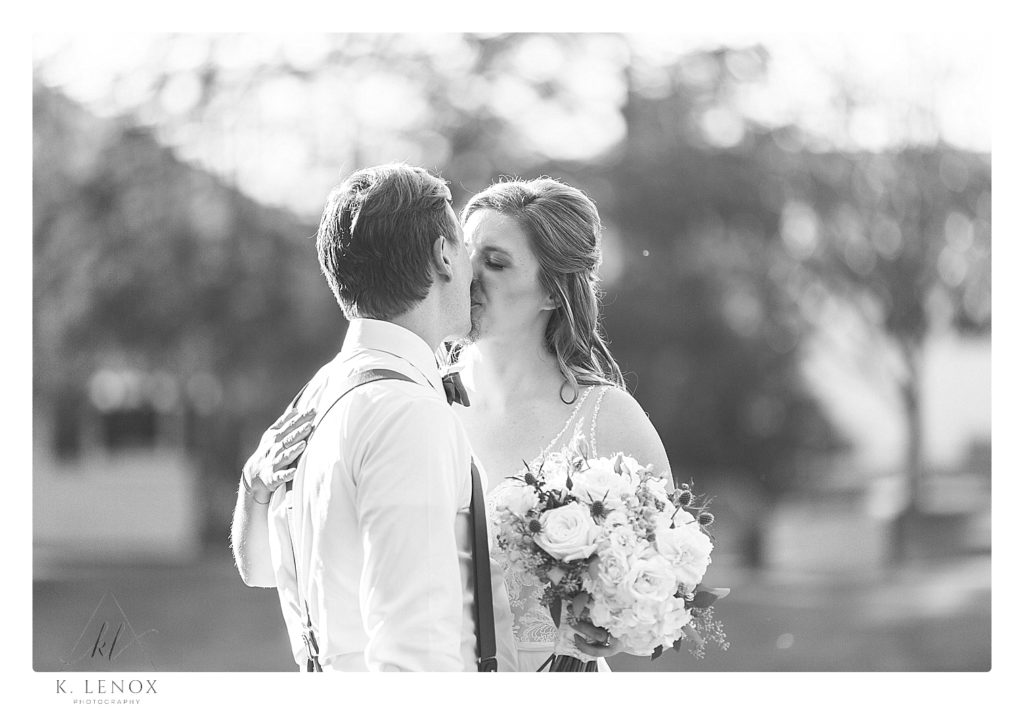 Black and white candid photo of a bride and groom kissing. 