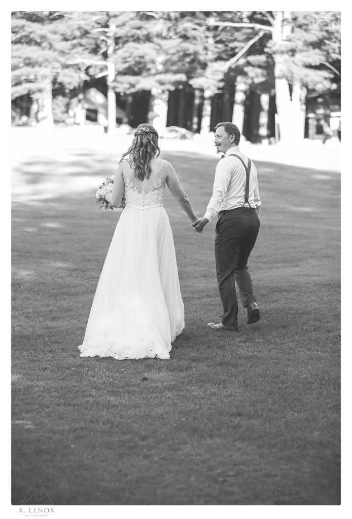Black and white candid photo of a bride and groom walking hand in hand on their wedding day. 