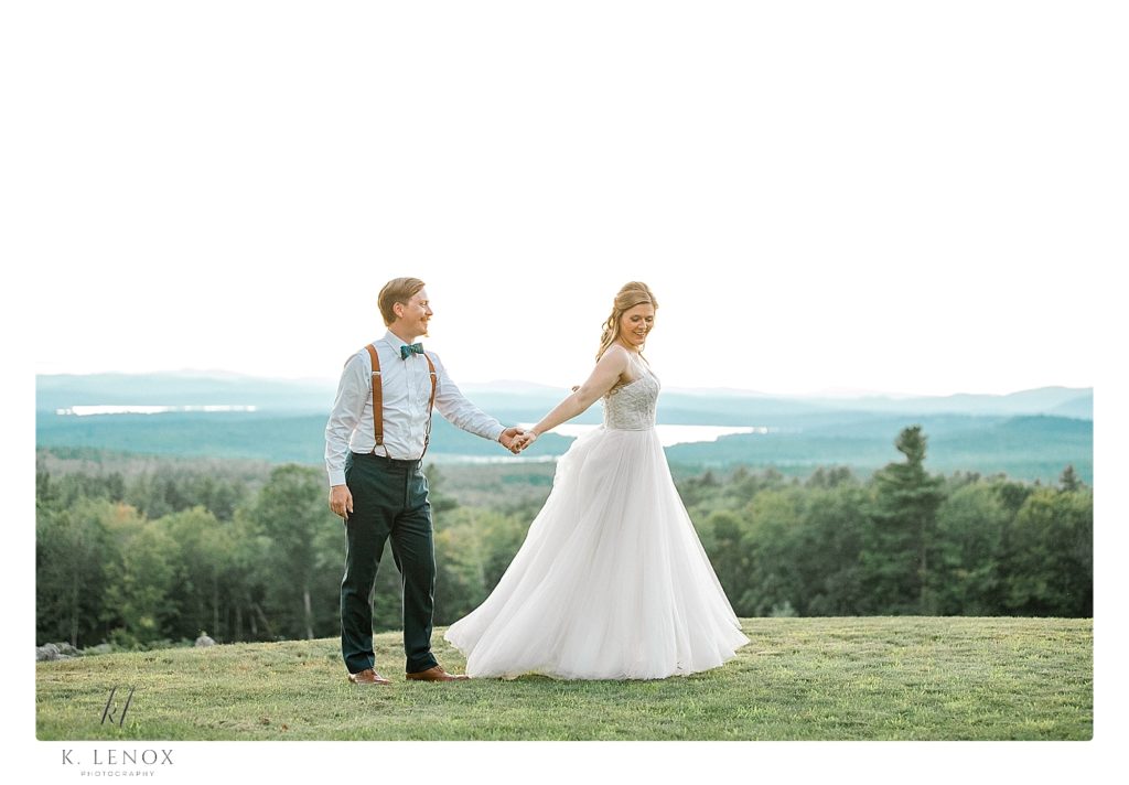 Bride and groom walk and hold hands while over looking the beautiful view of NH Mountains. 