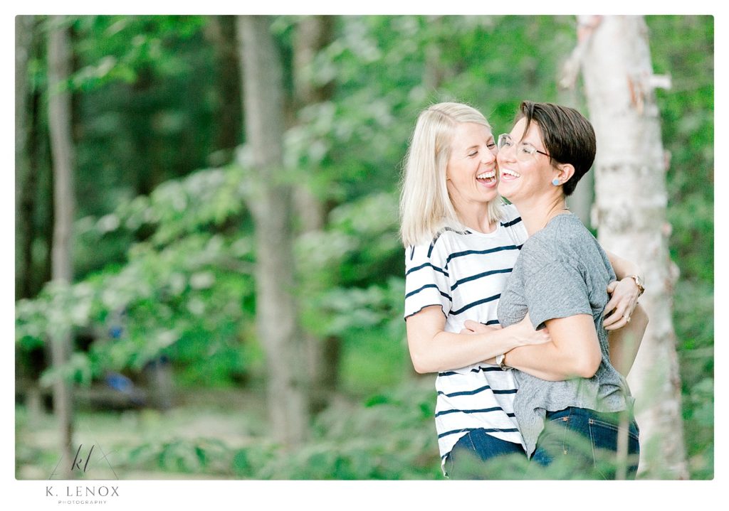 Candid moment of an Engaged same-sex couple laughing and hugging near Lake Sunapee. 