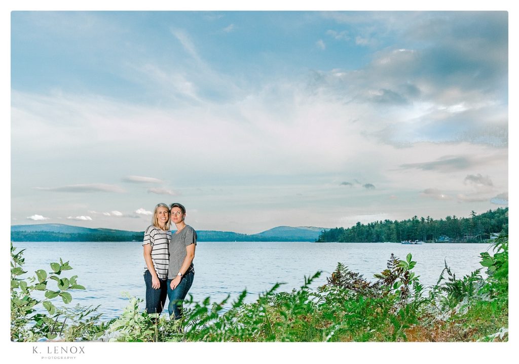 Engaged same sex couple pose for a formal portrait on the shore of Lake Sunapee during their engagement session with K. Lenox Photography. 