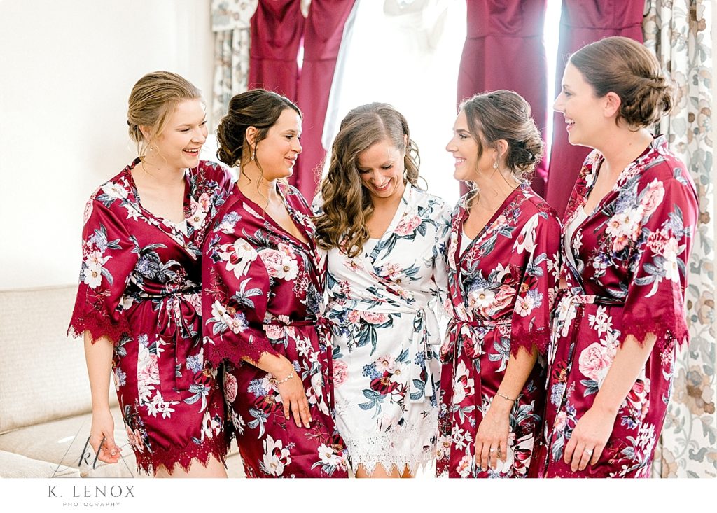 A bride wearing a white floral robe poses with her bridesmaids wearing maroon floral robes as they get ready for the Fall Wedding at The Mountain View Grand. 