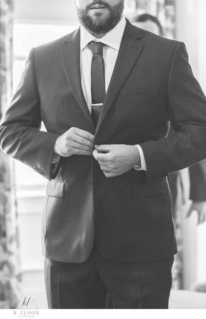 Black and White photo of a groom buttoning his suit jacket. 