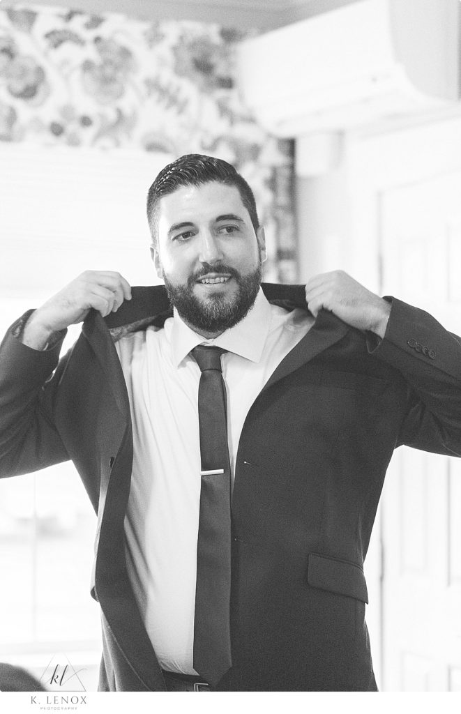Black and White photo of groom putting on his suit jacket as he gets ready on this wedding day. 