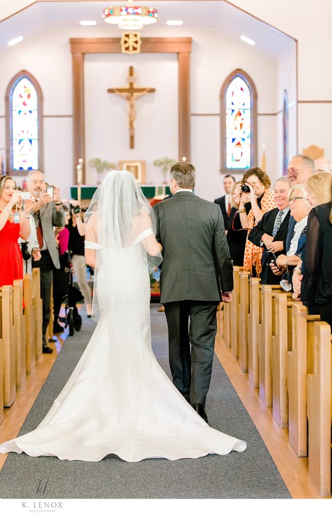 Picture taken from behind as a father walks his daughter down the aisle. 