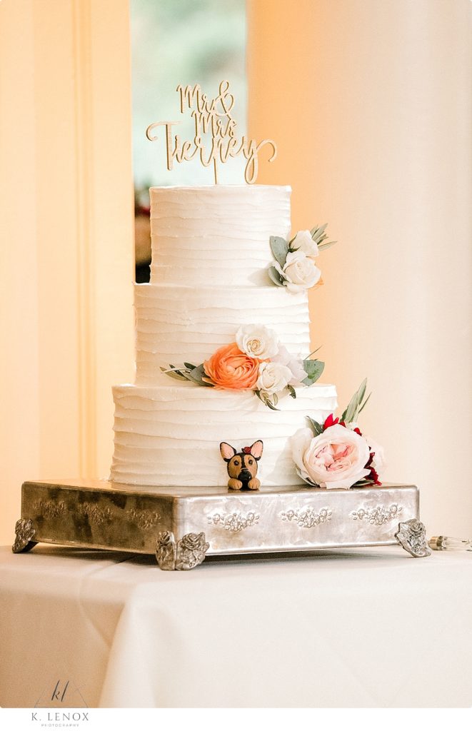 Simple three tiered wedding cake with white frosting and flowers. Little Dog custom decoration at the bottom. 