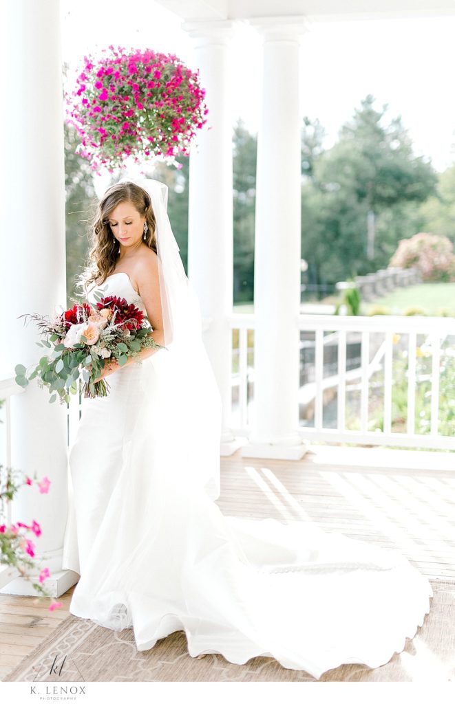 Picture showing a bride looking down at her floral bouquet on the porch of the Mountain View Grand on the first day of fall. 